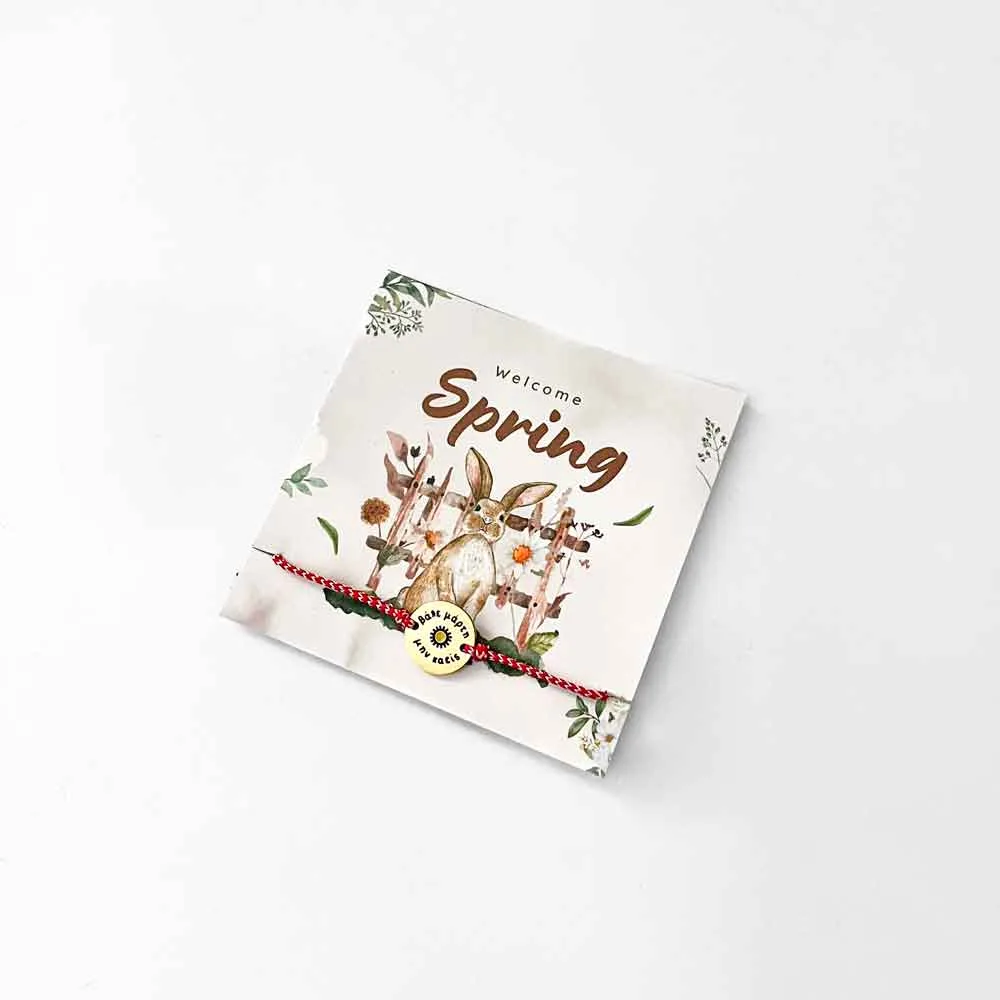 μαρτάκι a white square with a red string and a gold circle on it